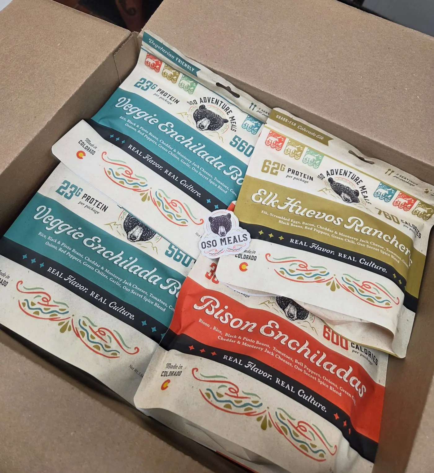 An open shipping box packed with Oso Veggie Enchilada Bowl, Elk Huevos Rancheros and Bison Enchiladas pouches