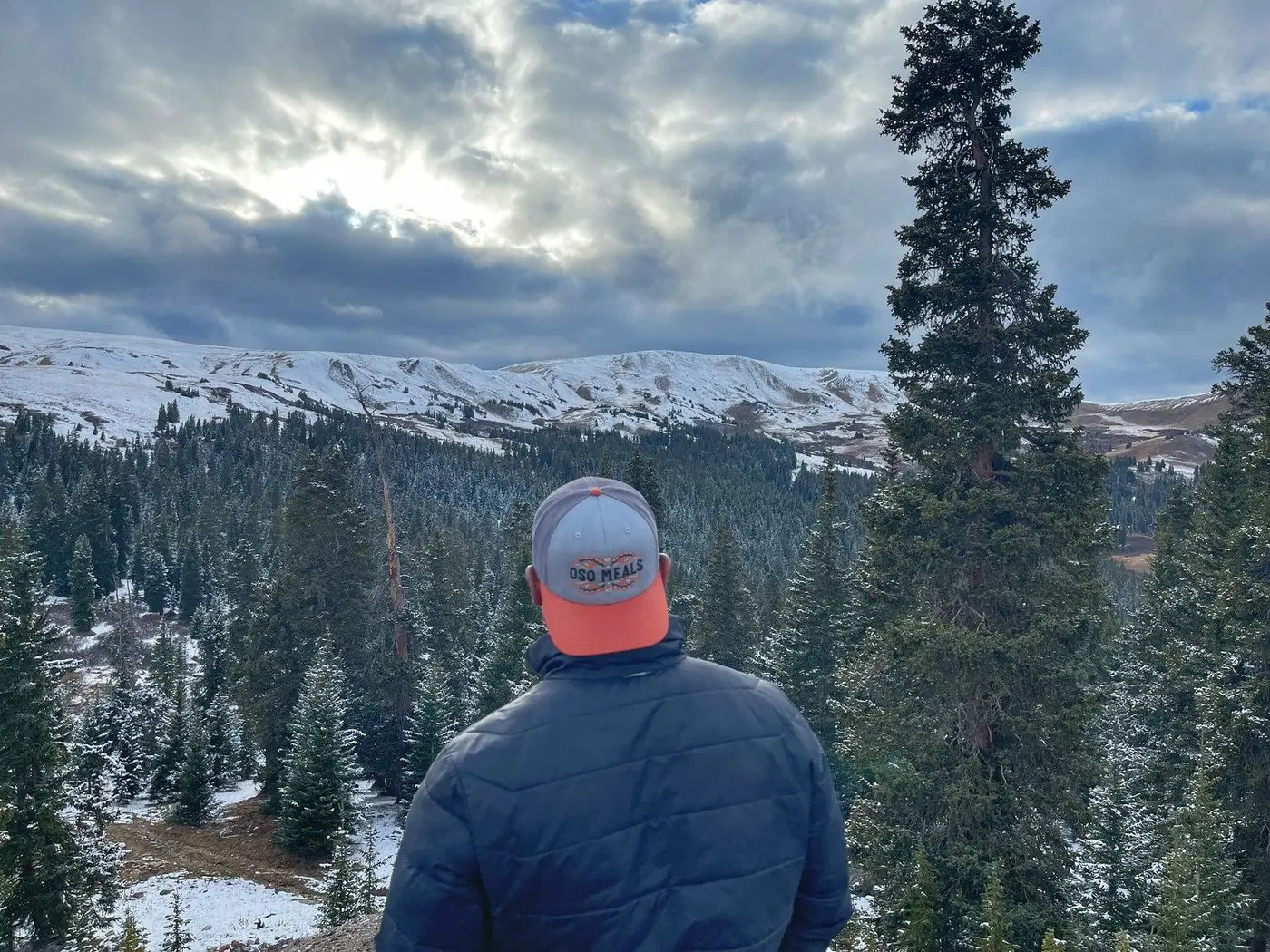 Hiker in an Oso cap looking out over snowy Colorado peaks