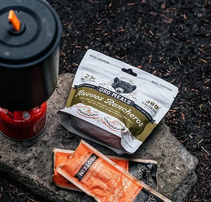 A backpacking pot and stove on a rock next to an Oso Huevos Rancheros pouch